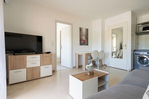 A modern living room with a flat-screen TV, a wooden cabinet, a coffee table, a grey sofa, and a washing machine. - L'Aparté Cannois avec balcon en centre-ville (Cannes)