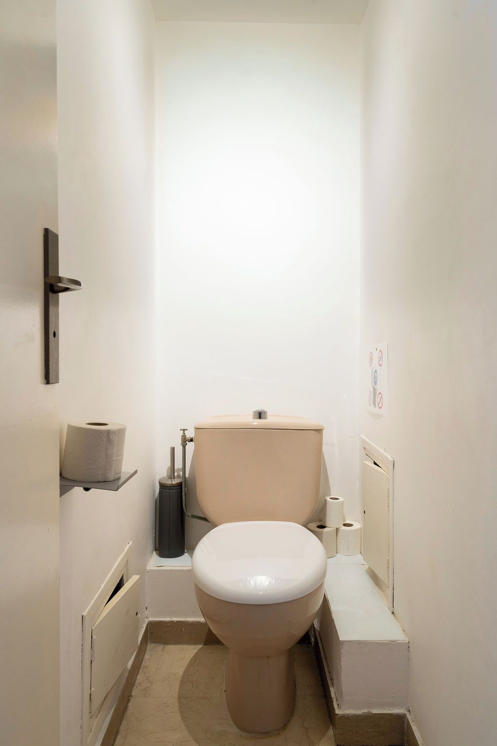 Ein kleines, weißes Badezimmer mit Toilette, einem Ablagefach mit Toilettenpapier und einer Toilettenbürste.
