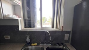 A kitchen with a double sink, a window with curtains, and a shelf above the sink.