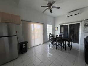 Une cuisine équipée d’un réfrigérateur, d’un ventilateur de plafond, d’une table à manger avec des chaises et d’une porte-fenêtre coulissante.