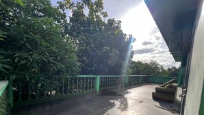A covered outdoor area with a tiled floor, a green railing, and a sofa.