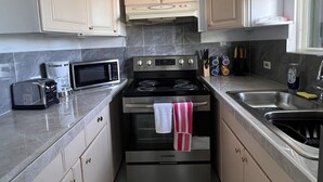 A compact kitchen with a built-in microwave, toaster, and stove, featuring light-colored cabinets and a tiled backsplash.