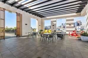 A rooftop terrace with a city skyline view, featuring outdoor seating and potted plants.