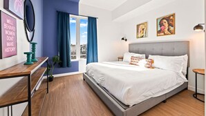 Ein modernes Schlafzimmer mit einem großen Bett, einem Schreibtisch, einem Fenster mit Vorhängen und Bildern an den Wänden.