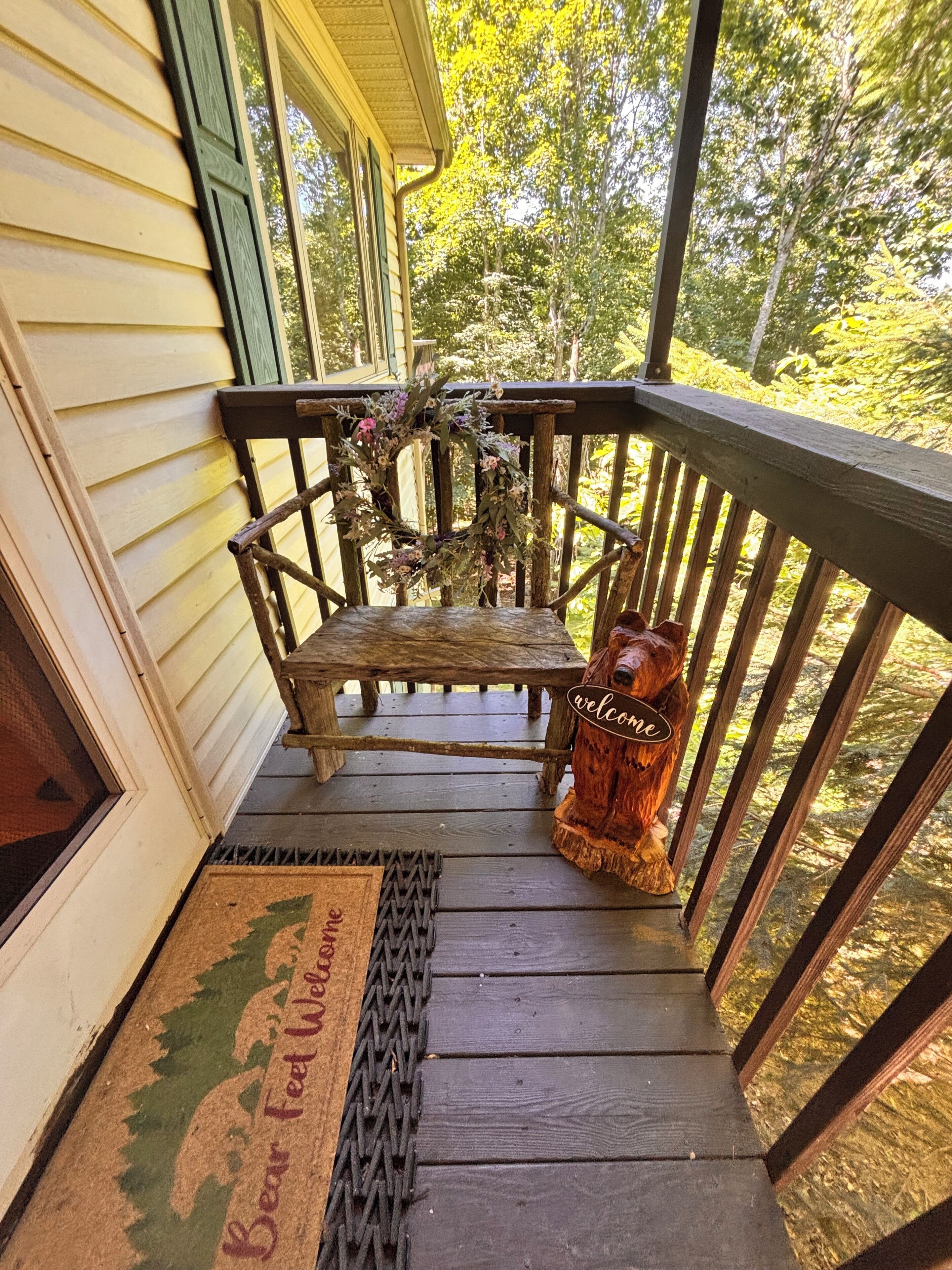 A wooden porch with a bench, a welcome sign, and a doormat.