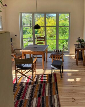 Ein Zimmer mit einer großen Schiebeglastür, die zu einem Garten führt, einem Holzespeisetisch mit Stühlen und einem gemusterten Teppich auf dem Boden.