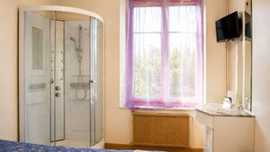 Une chambre à coucher comprenant un lit, une douche, une fenêtre avec des rideaux, une télévision et une petite salle de bain.