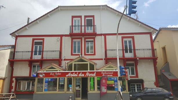Un immeuble de deux étages à la façade rouge et blanche, comprenant un bar, un restaurant et un hôtel appelé « Hôtel du Nord ».