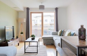 Ein modernes Wohnzimmer mit einer Couch, einem Couchtisch, einem Fernseher und einem großen Fenster mit Vorhängen.