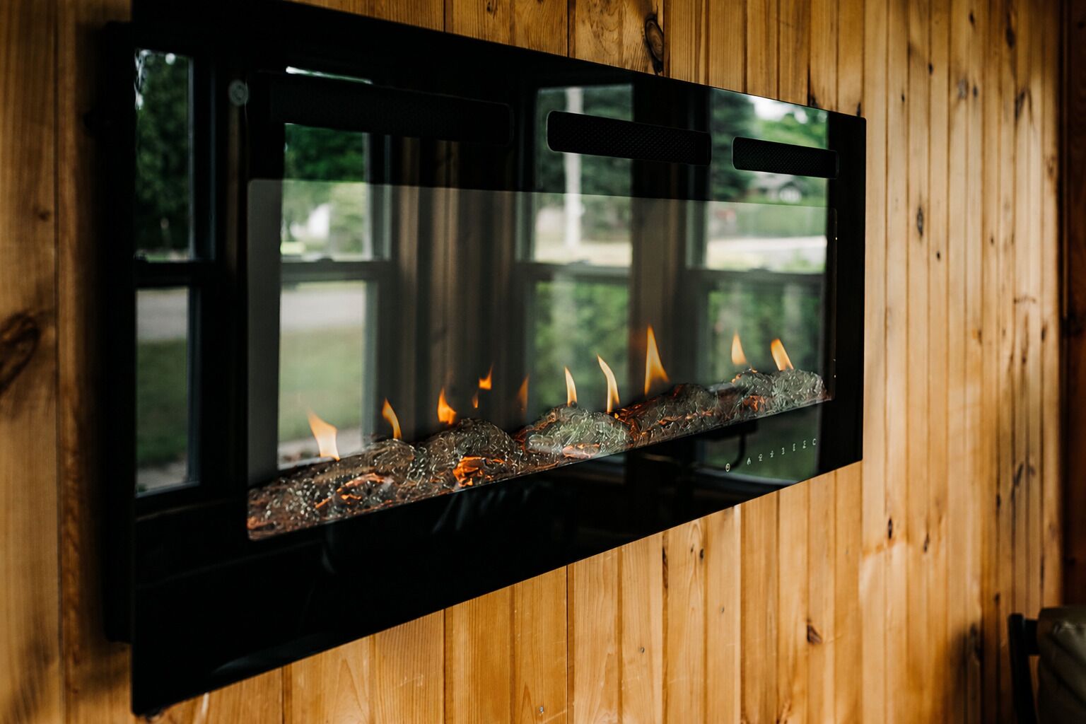 A fireplace with a glass front, set against a wooden wall.