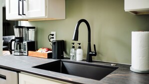 A kitchen with a black sink, a coffee maker, and two soap dispensers. - 2 king beds w/private baths •firepit •walk to town and Lake Charlevoix (Boyne City)