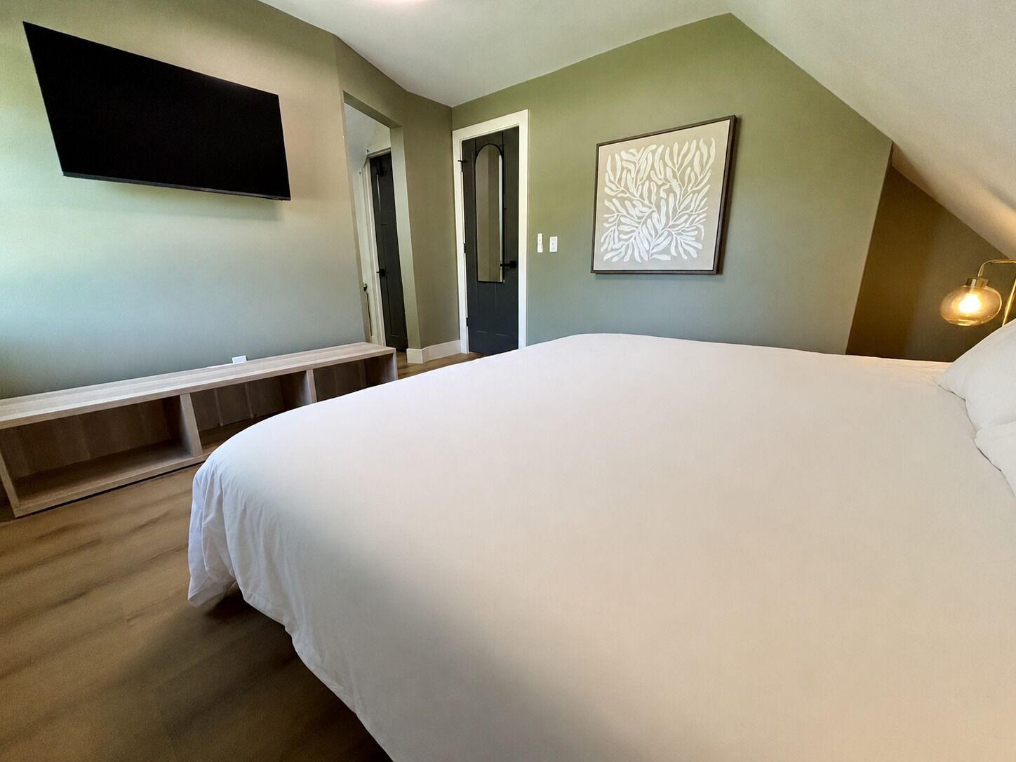 Ein Schlafzimmer mit einem großen Bett, einer Bank, einem Flachbildfernseher und einem gerahmten Kunstwerk an der Wand.