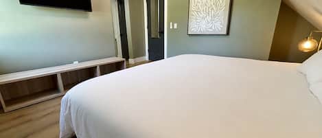 Un dormitorio con una cama grande, un banco, un televisor de pantalla plana y una obra de arte enmarcada en la pared.