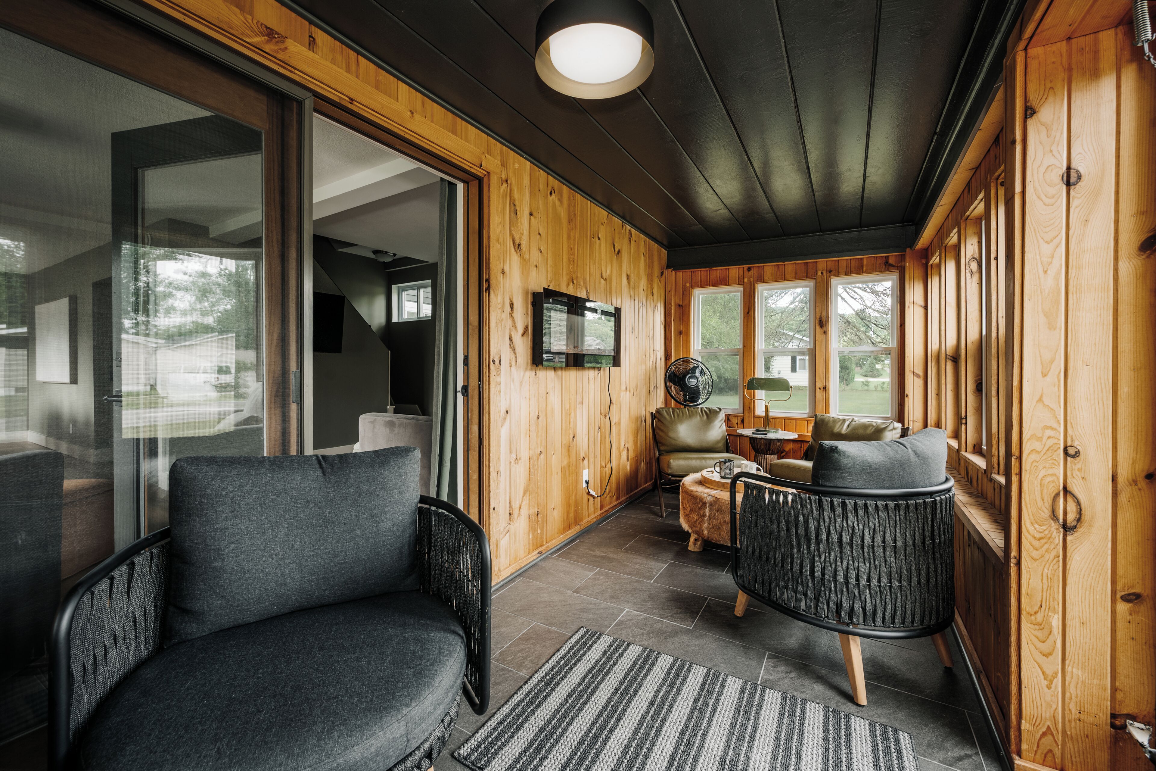A cozy cabin interior with a large sliding glass door, a wooden ceiling, and a seating area with two chairs and a small table.