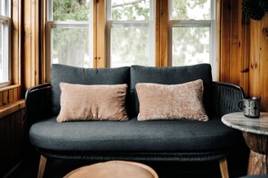 Ein dunkelgraues Sofa mit zwei hellbraunen Kissen vor einer Wand aus Holzverkleidung mit großen Fenstern.