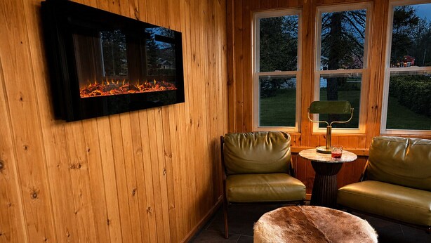 A cozy room with a fireplace, two leather chairs, a round table with a lamp, and a fur ottoman. - 2 king beds w/private baths •firepit •walk to town and Lake Charlevoix (Boyne City)