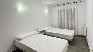 A room with two beds, a ceiling light, a power outlet, and a window with curtains. - Apartment in the village of Riglos, at the foot of the Mallos de Riglos (Riglos)