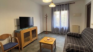 A living room with a sofa, a television on a wooden cabinet, a small table, a chair, and a floor lamp. - Apartment in the village of Riglos, at the foot of the Mallos de Riglos (Riglos)