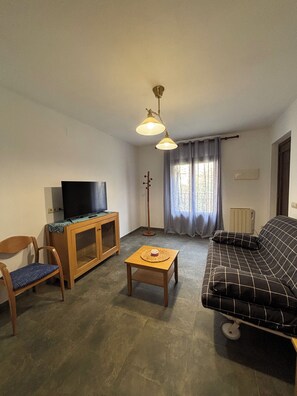 A living room with a sofa, a television on a wooden cabinet, a small table, a chair, and a floor lamp. - Apartment in the village of Riglos, at the foot of the Mallos de Riglos (Riglos)