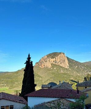 A mountain with a clear sky, a tall tree, and buildings with red-tiled roofs.