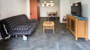 A living room with a sofa, a wooden dining table, a TV, and a ceiling light fixture. - Apartment in the village of Riglos, at the foot of the Mallos de Riglos (Riglos)