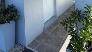 Eine weiße Tür mit der Nummer 2159 darüber, ein kleiner Blumentopf zur Linke und ein gefliester Weg, der zur Tür führt.