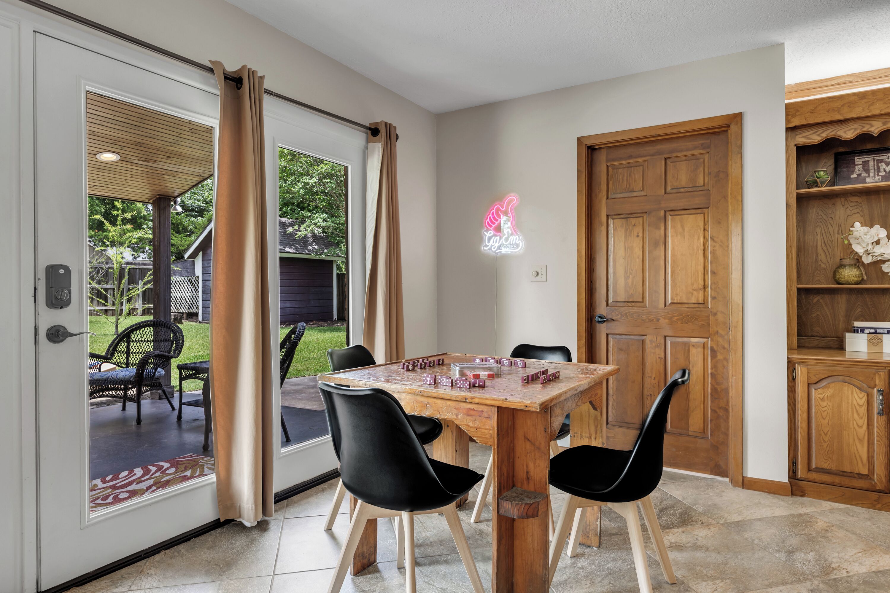 Un comedor con mesa de madera, sillas negras y vista al patio trasero a través de un ventanal.