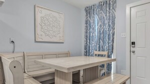 Una habitación con un banco de madera, una mesa, una cortina estampada y una puerta.