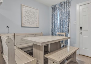 Ein Zimmer mit einer Holzbank, einem Tisch, einem gemusterten Vorhang und einer Tür.