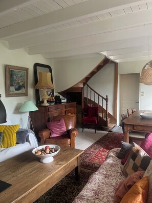 Ein gemütliches Wohnzimmer mit einem Holztisch, einer Couch, einem roten Sessel und einer Treppe, die in einen anderen Raum führt.