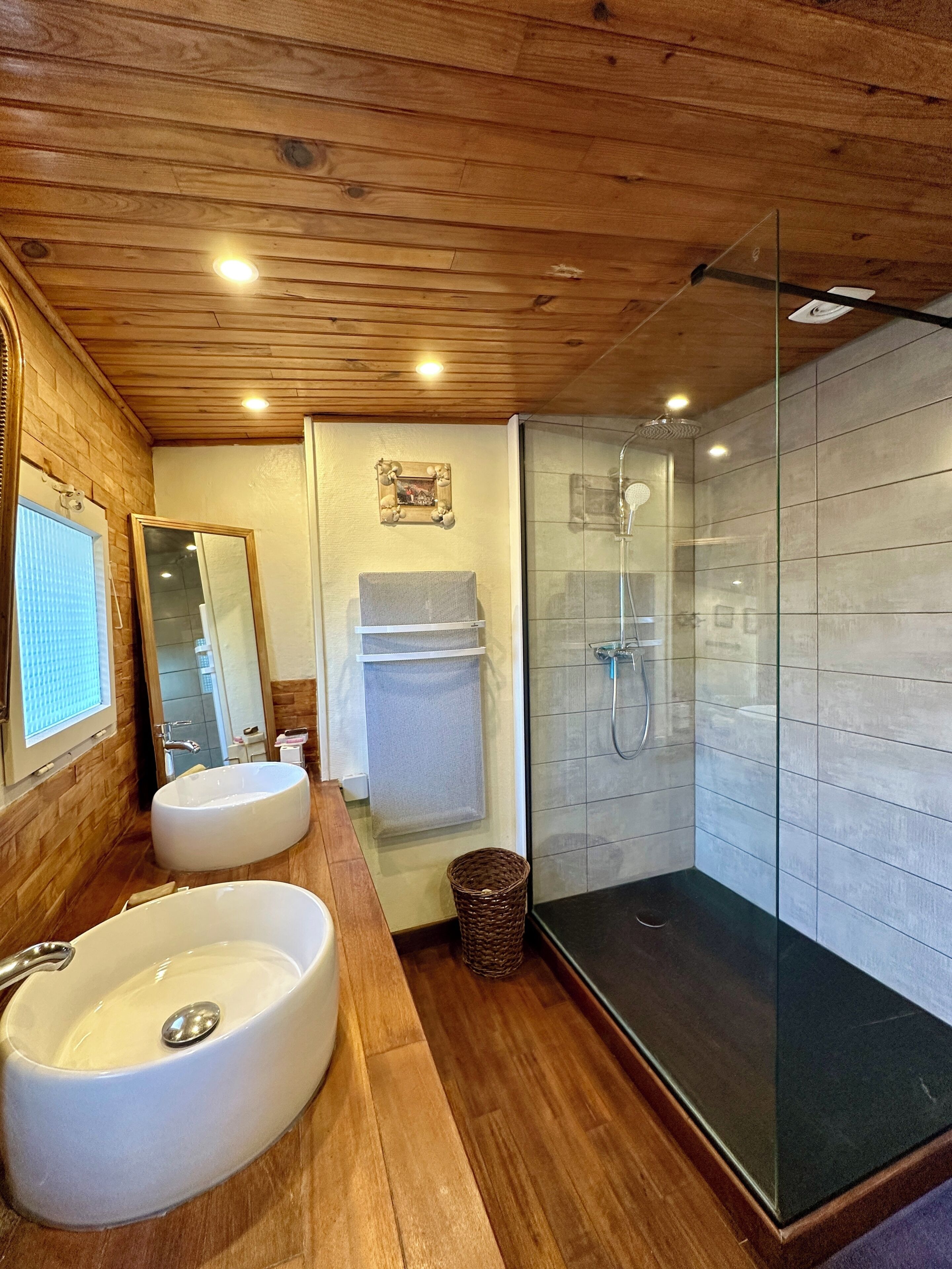 A bathroom with wooden walls, a large sink, a mirror, a shower, and a towel rack.