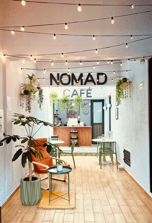 Interior acolhedor de um café com chão de madeira, balcão de bar e plantas penduradas.