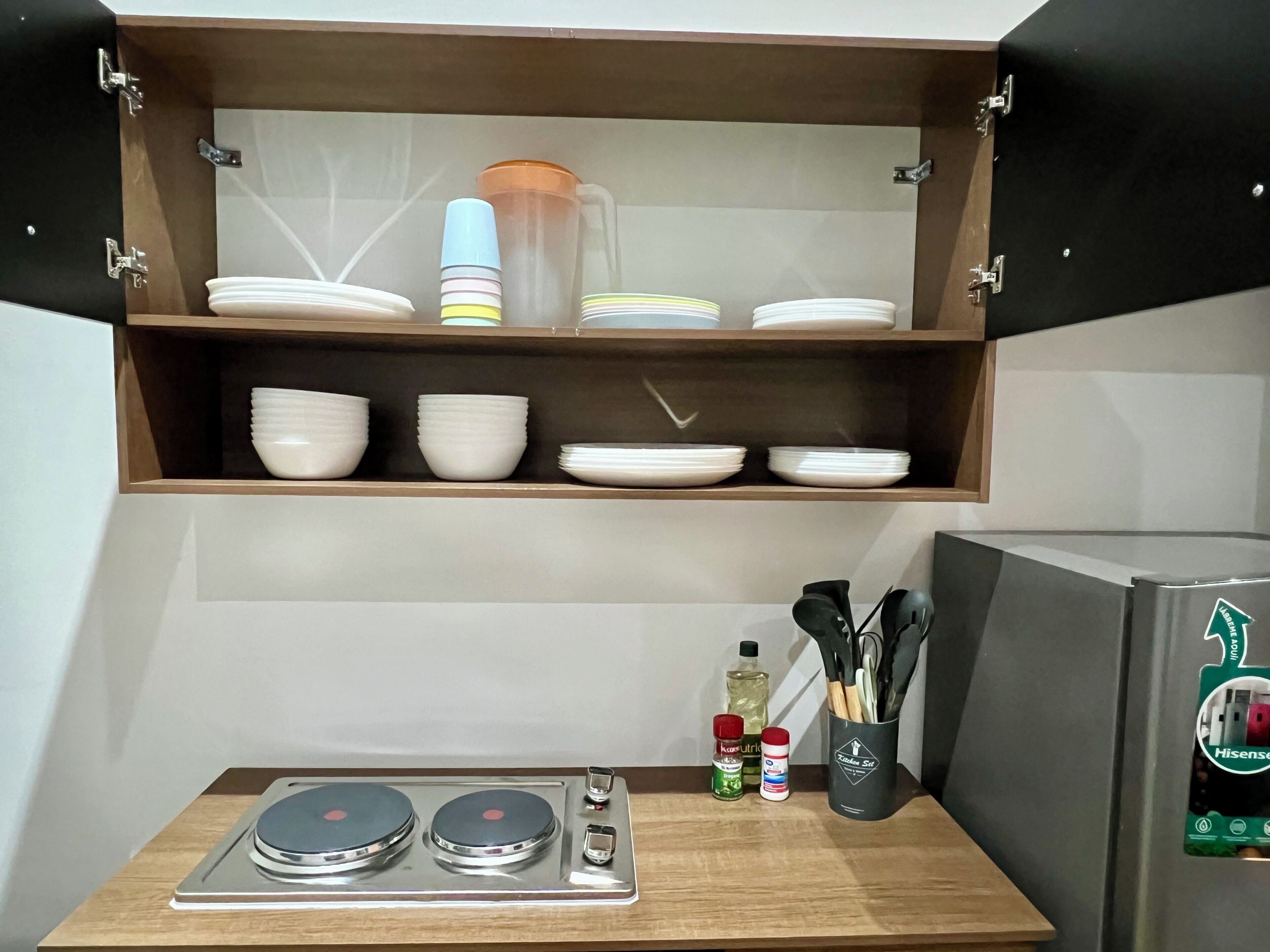 A kitchen with a wooden cabinet shelf holding white plates and bowls, a stainless steel stove, and a utensil holder.