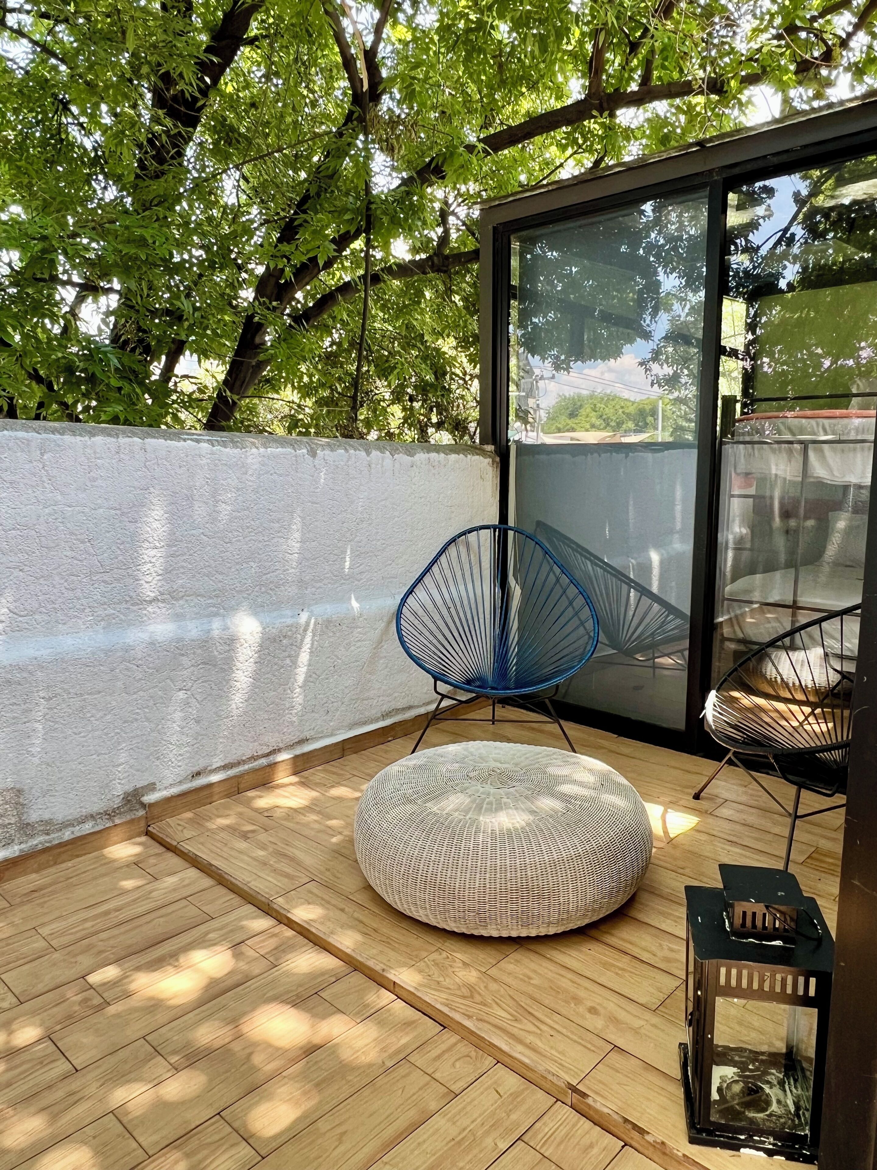 A modern outdoor seating area with a round wicker ottoman, a blue wire chair, and a black metal chair.