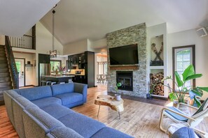 Ein modernes Wohnzimmer mit Kamin aus Stein, einem großen Fernseher und einem blauen Ecksofa.