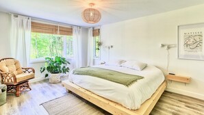 Een slaapkamer met een bed, een stoel, een plant en een wanddecoratie.