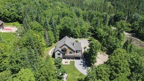 A single-story house surrounded by dense forest, with a visible driveway and a small patio area. - A rustic cabin near a lake, 45 minutes from Quebec City—perfect for families! (Saint-Raymond)