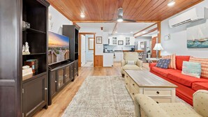 A living room with a wooden ceiling, a sofa, a coffee table, and a TV. - Coco Cottage w Outdoor Bar and TV Walk to Beach (North Myrtle Beach)