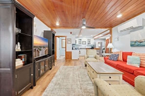 A living room with a wooden ceiling, a sofa, a coffee table, and a TV. - Coco Cottage w Outdoor Bar and TV Walk to Beach (North Myrtle Beach)