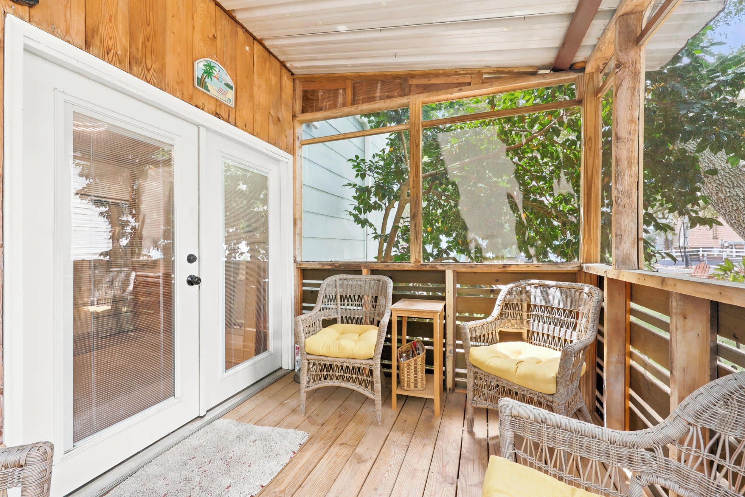 A covered porch with wicker furniture, a wooden table, and a glass door.