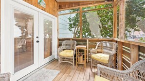A covered porch with wicker furniture, a wooden table, and a glass door. - Coco Cottage w Outdoor Bar and TV Walk to Beach (North Myrtle Beach)