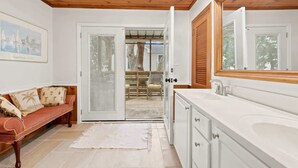A bathroom with a large mirror, white cabinetry, and a wooden ceiling. - Coco Cottage w Outdoor Bar and TV Walk to Beach (North Myrtle Beach)