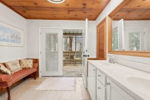 A bathroom with a large mirror, white cabinetry, and a wooden ceiling. - Coco Cottage w Outdoor Bar and TV Walk to Beach (North Myrtle Beach)