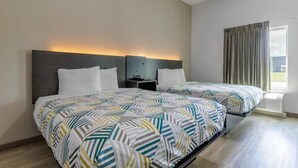 Ein Hotelzimmer mit zwei Betten, einem Nachttisch, einem Fenster mit Vorhängen und einem Kopfteil mit integrierter Beleuchtung.