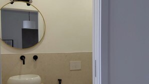 A bathroom with a round mirror, a white sink, a toilet, and a shower.