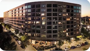 A multi-story hotel with a curved facade, outdoor seating area, and a visible entrance with signage.