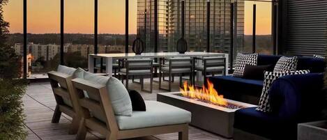 An outdoor terrace with a fire pit, seating, and a view of the cityscape.