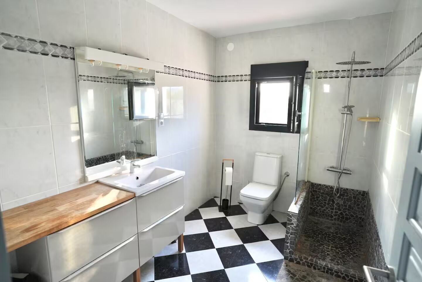Une salle de bain avec un carrelage à motifs géométriques, des toilettes, un lavabo et une douche.