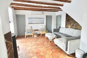 A cozy living room with a grey sofa, two armchairs, a small table, and a stone wall. - Large Family Villa in L'Ametlla de Mar – Spacious Garden, Bar, and Pool (L'Ametlla de Mar)