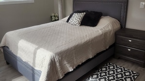 Une chambre à coucher avec un lit, une table de chevet, une lampe et une œuvre d’art accrochée au mur.